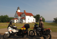 2 motorcycles parked in front of a lighthouse with water in the distance